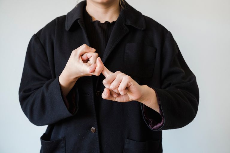 A close-up view of a person making a sign language gesture against a white studio background.